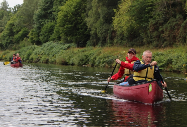  Padre e hijo con ayudas a la flotabilidad amarillas recorriendo el lago en canoa